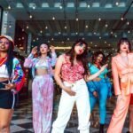 A diverse group of stylish young adults posing confidently under string lights indoors.