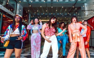 A diverse group of stylish young adults posing confidently under string lights indoors.